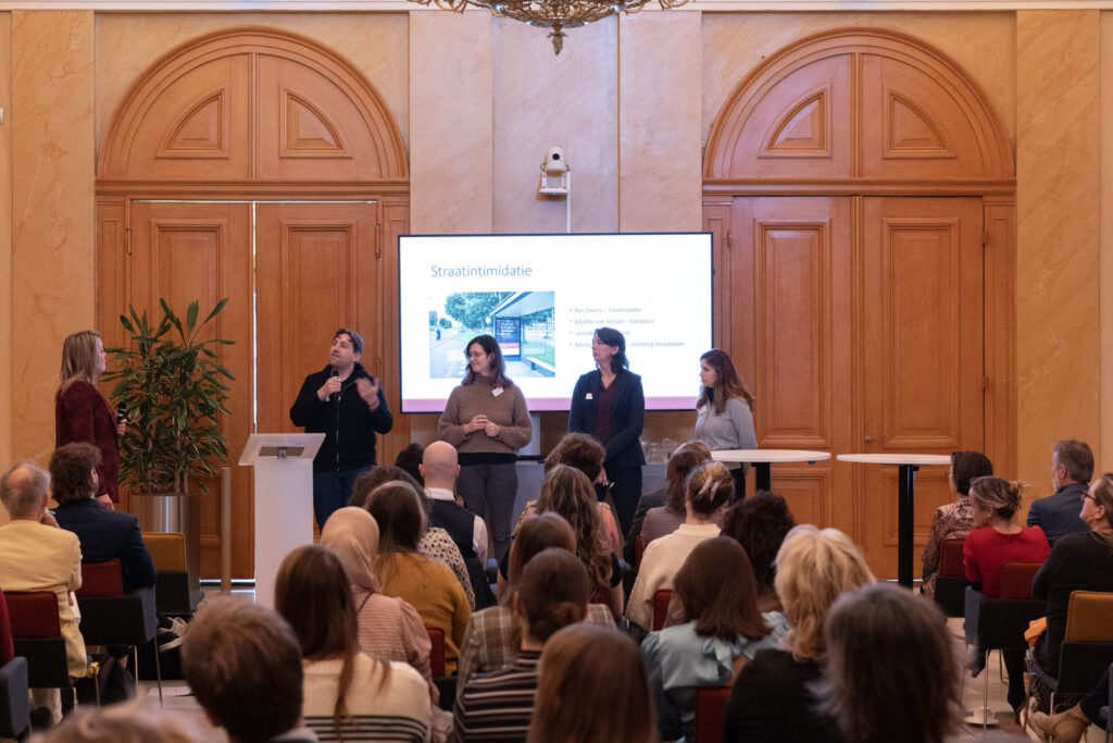 Vier mensen, waaronder Myrthe van Gestel, staan voor een scherm, ze geven een presentatie.